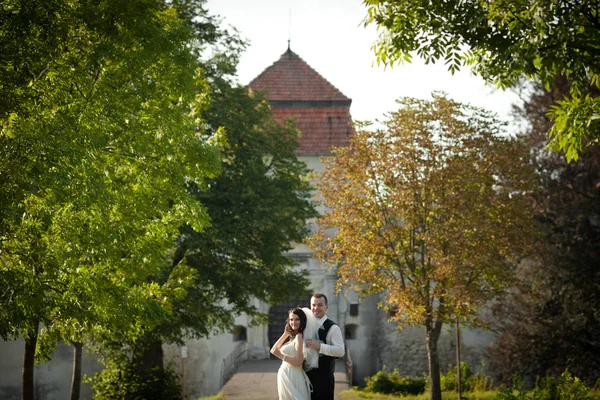 Groom segura o véu da noiva enquanto está atrás dela no castelo — Fotografia de Stock
