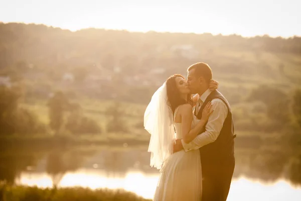 Imagen cálida de la pareja de boda besándose ante el lago en el li —  Fotos de Stock