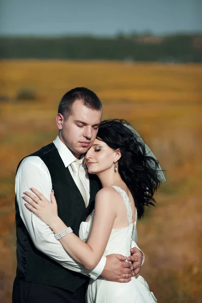 Groom fecha os olhos abraçando uma noiva no campo — Fotografia de Stock