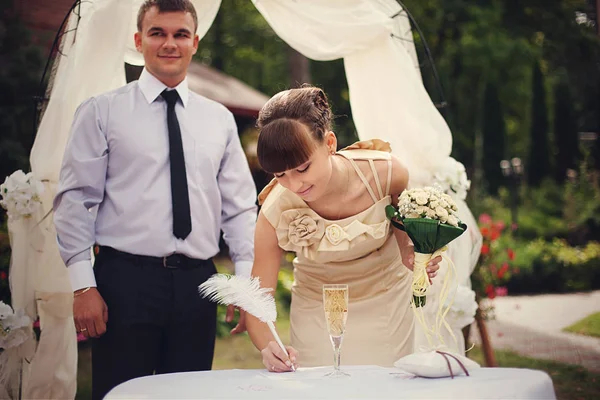 Beautiful bride signs wedding documents with a feather — Stock Photo, Image