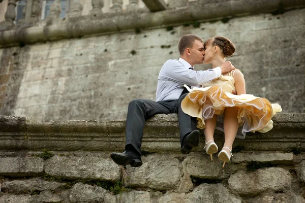 Young man kisses a woman in evening hown sitting on the stone — Stock Photo, Image