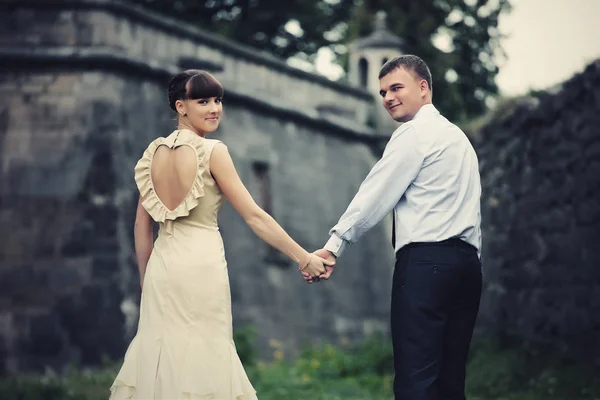 Bride and groom look over their shoulders walking around an old — Stock Photo, Image
