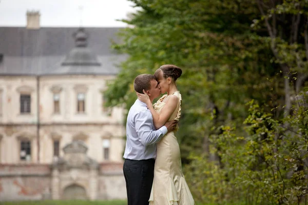 A tender kiss of a stylish couple standing under the green trees — Stock Photo, Image