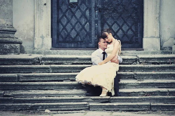 Tender lady sits on groom's knees while they pose on ruined foot — Stock Photo, Image