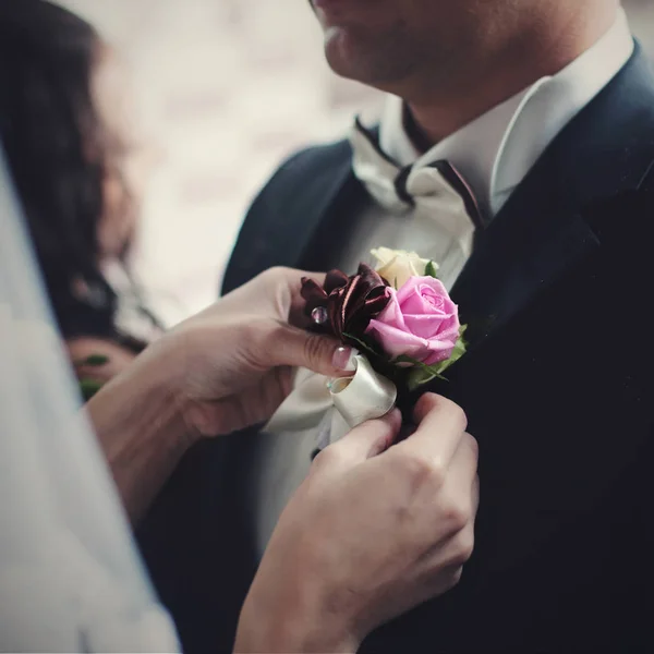 Delicte bride 's hands pin pink and violet boutonniere to groom' s — стоковое фото