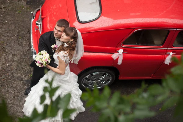 Casal de casamento elegante posa atrás de um velho carro vermelho — Fotografia de Stock