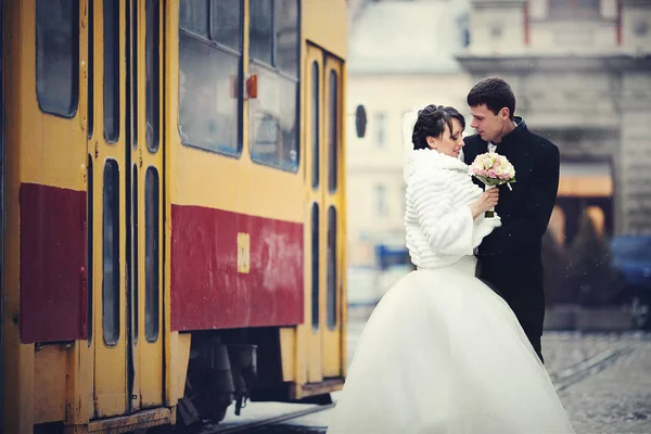 Sposo abbraccia una sposa in cappotto invernale mentre tram guida dietro t — Foto Stock