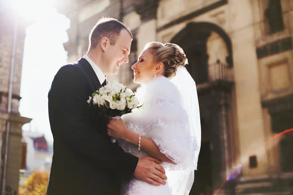 Усміхнена весільна пара стоїть у променях сонця перед замком — стокове фото
