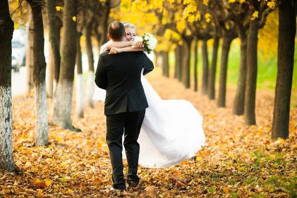 Bräutigam wirbelt eine glückliche Braut auf dem Weg voller fallender Blätter — Stockfoto