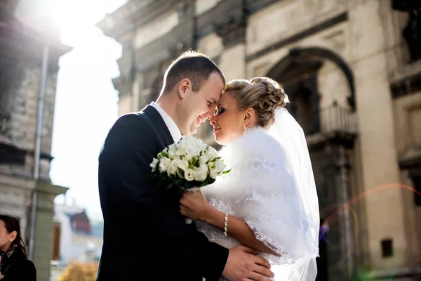 Bruidegom glimlacht mooie bruid knuffelen in de stralen van de ochtendzon — Stockfoto