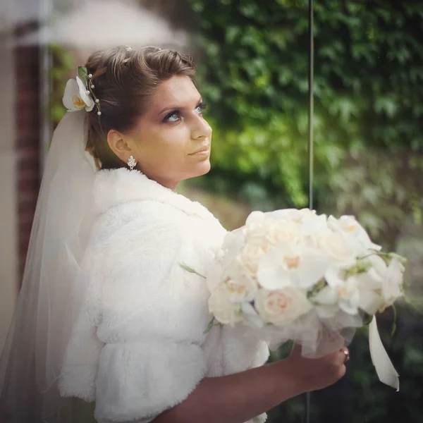 Blond brud i päls håller ett bröllop bukett stående utanför — Stockfoto