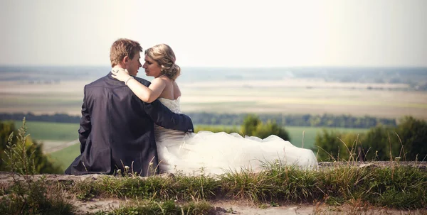 Braut und Bräutigam schauen sich im Gras sitzend in die Augen — Stockfoto