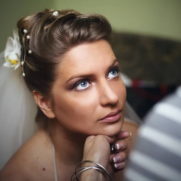 Bride with deep blue eyes looks up while woman checks her make u