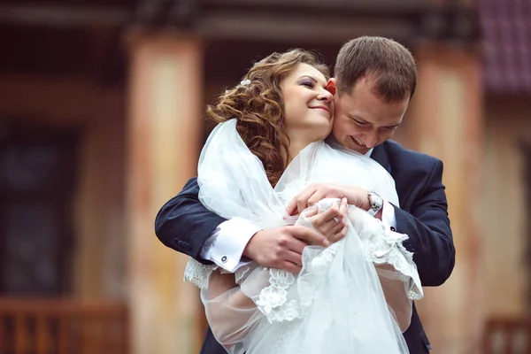 Bruden lutar till brudgummens kind medan han kramar henne bakifrån — Stockfoto