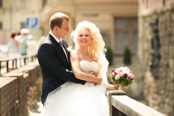 Sposo abbracci bella sposa riccia in piedi sul ponte — Foto Stock