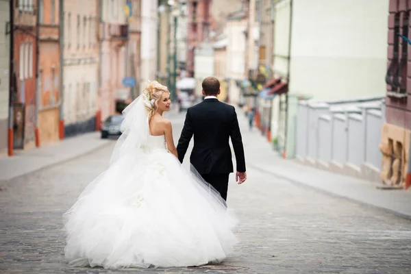 Divertida novia mira por encima de su hombro caminando con un novio en negro — Foto de Stock