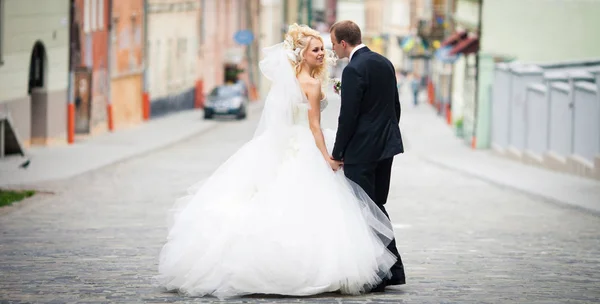 Sposa bionda con lunghi riccioli tiene la mano dello sposo mentre cammina — Foto Stock