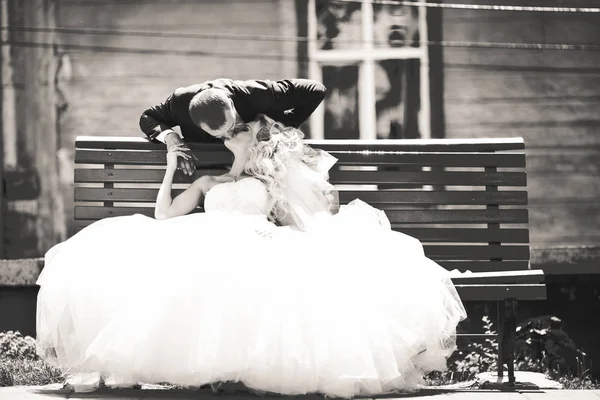 Brudgummen böjer sig över till bruden medan hon vilar på bänken — Stockfoto
