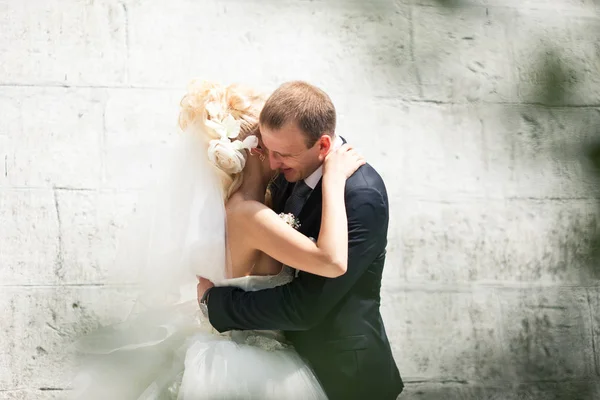 Sposo abbracci sposa strettamente in piedi alla luce del sole dietro un bianco — Foto Stock