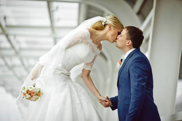 Невеста достигает лица жениха для поцелуя стоя на скамейке — стоковое фото