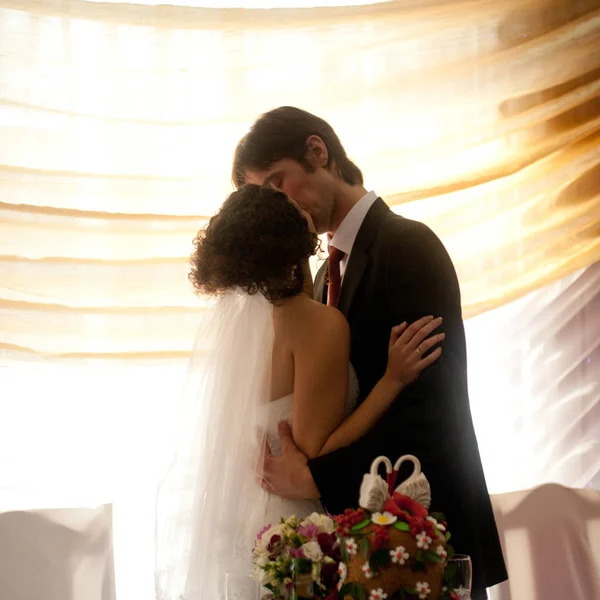 Beauriful wedding couple kisses in the front of a bright window — Stock Photo, Image