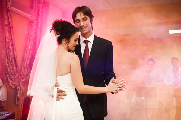 Groom smiles while dancing with a curly bride in pink light — Stock Photo, Image