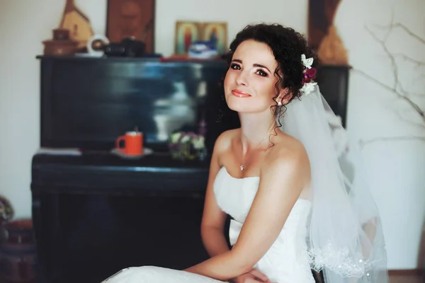 Splendida sposa con pelle lucente e capelli ricci si siede nella stanza — Foto Stock