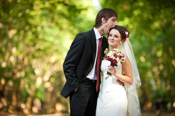 Sposo cerca di mordere la testa della sposa in piedi nella foresta — Foto Stock