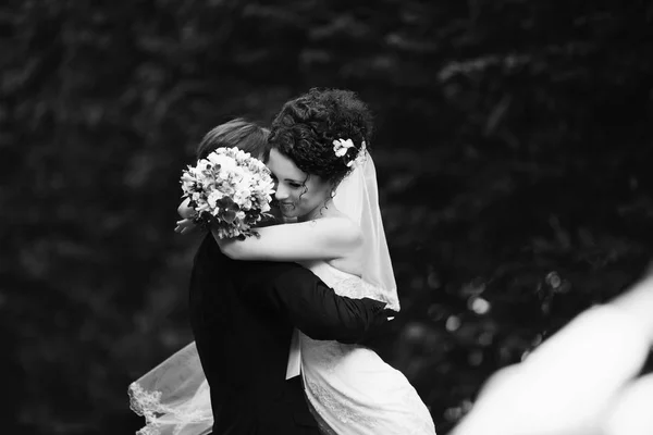Curly bride leans to groom's shoulder while he whirls her in the — Stock Photo, Image