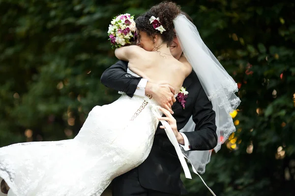 El velo de la novia cubre la cara del novio mientras él la gira en el parque — Foto de Stock