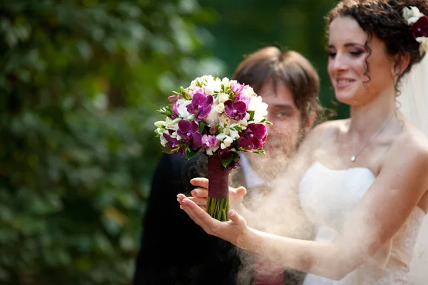 Sposo soffia con un fumo sopra il bouquet di nozze tenuto da un ibrido — Foto Stock