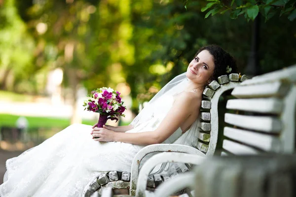 Dolce sposa riposa su una panchina bianca nel parco — Foto Stock