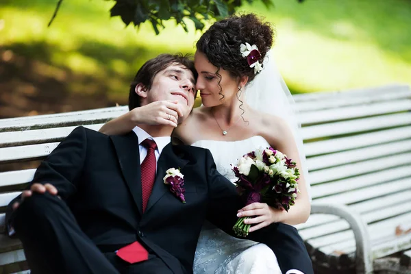 Groom repousa sobre o ombro da noiva enquanto eles se sentam no banco — Fotografia de Stock