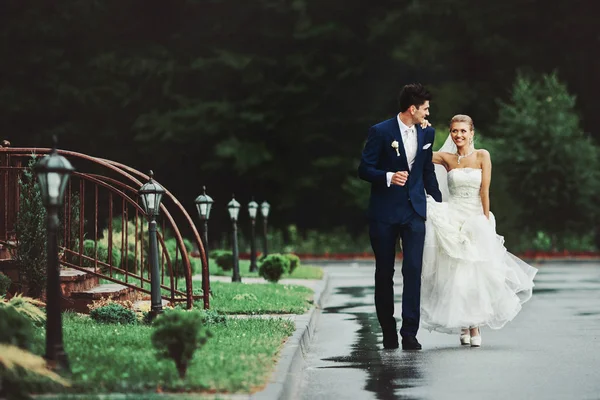 Высокий жених в синем костюме идет с красивой невестой на мокром — стоковое фото