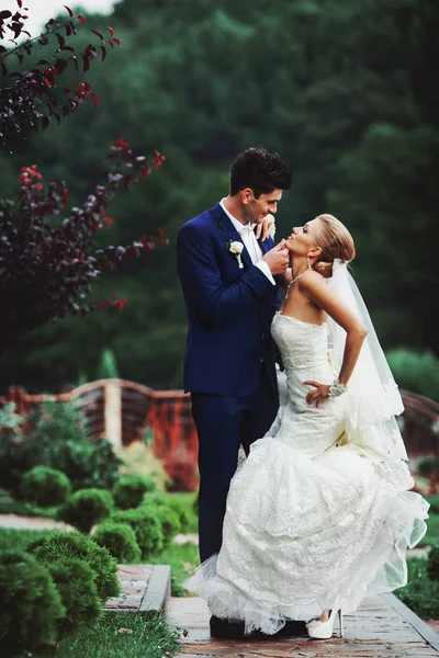 Bräutigam hält Braut bewundernd im Garten am Kinn — Stockfoto