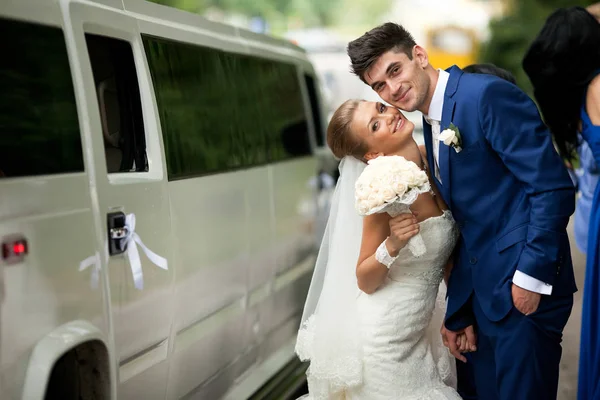Bonita novia se inclina a un novio de pie detrás de una limusina blanca —  Fotos de Stock