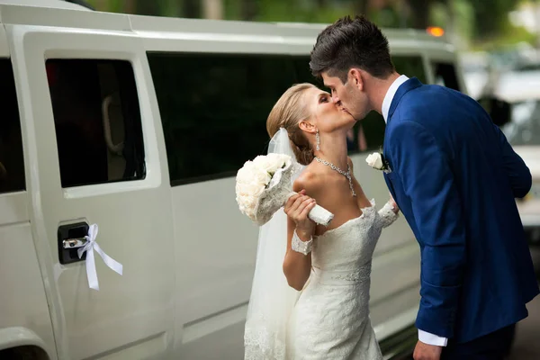 Brünette Bräutigam küsst eine winzige Braut, die vor einer reichen Limousine steht — Stockfoto
