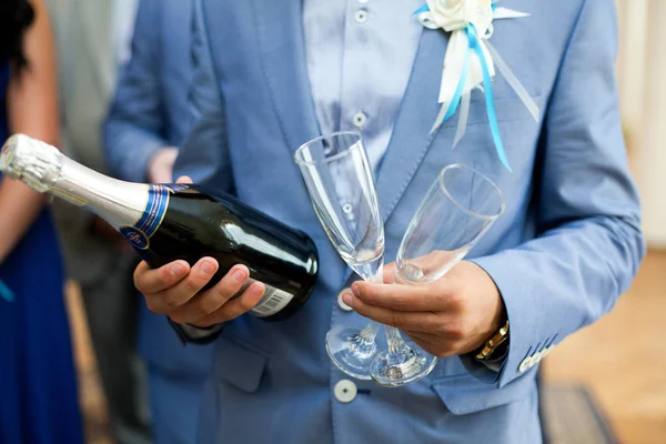 Man in licht blauw pak houdt een fles champagne en twee glazen — Stockfoto