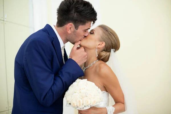 Groom beija uma noiva linda de pé em uma sala branca — Fotografia de Stock