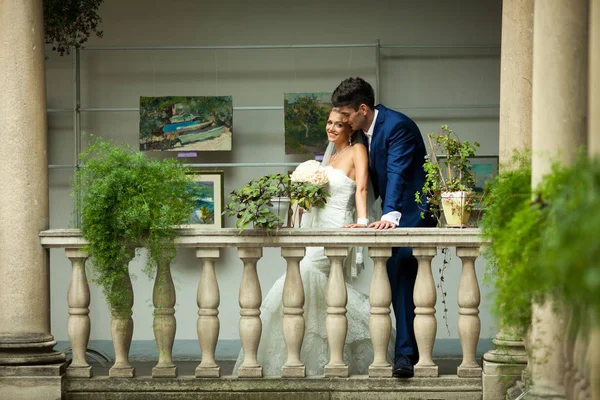Alto noivo inclina-se sobre uma noiva minúscula enquanto posando no velho balco — Fotografia de Stock