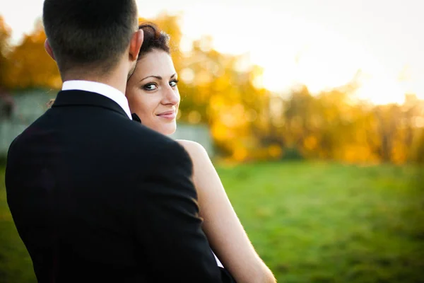 Brunette bride looks over groom's shoulder while standing on the — Stock Photo, Image