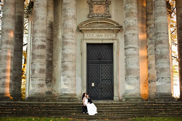 Νύφη στηρίζεται στα γόνατά του γαμπρού ενώ κάθονται πίσω από μια παλιά πέτρινη c — Φωτογραφία Αρχείου