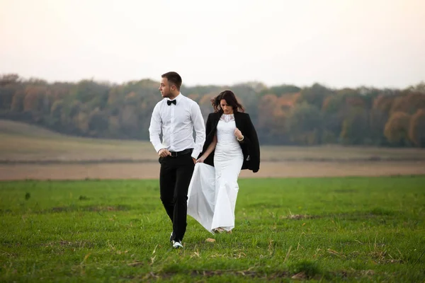 Elegante novio camina con una novia vestida con su chaqueta — Foto de Stock