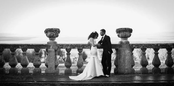 Brudgummen ser ut på en snygg brud medan poserar på gamla balkongen — Stockfoto