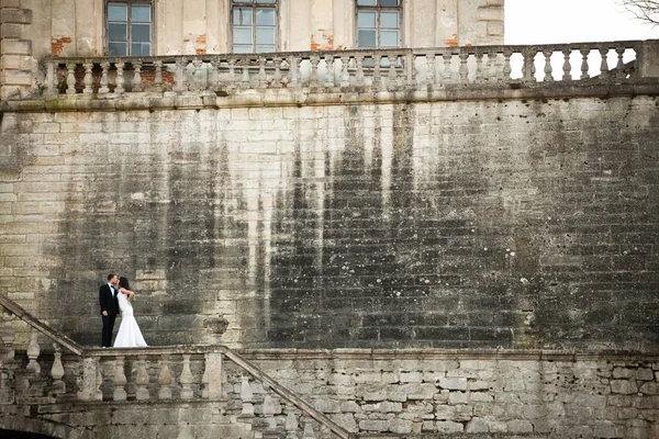 En titt på avstånd på en brud som kysser en brudgum som står på ston — Stockfoto