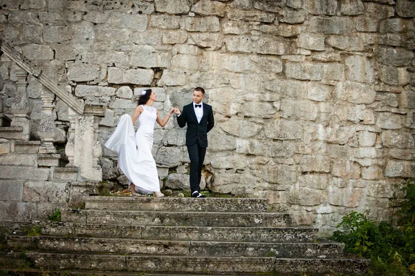 Gentle groom helps bride to walk down the stone stairs — Stock Photo, Image