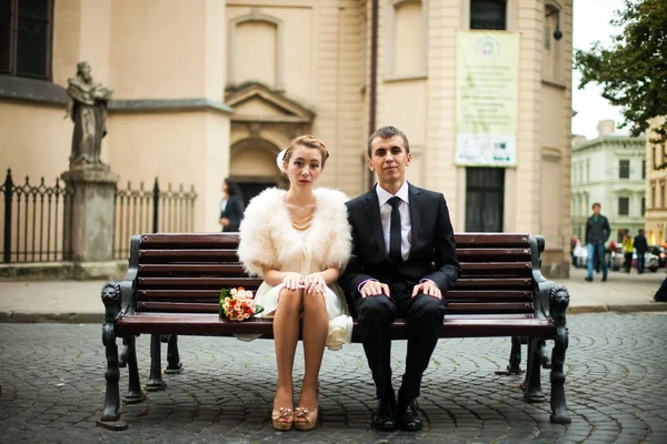 Stylish newlyweds sit straight on the bench
