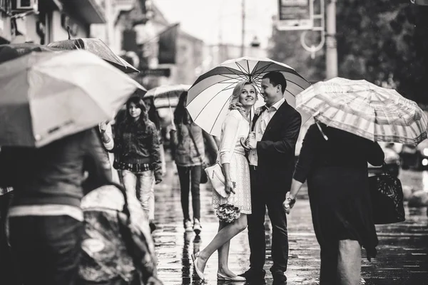 Casal de casamento sorridente fica na multidão sob um guarda-chuva — Fotografia de Stock