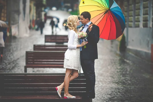 Bruid en bruidegom staan onder de paraplu op de Bank — Stockfoto
