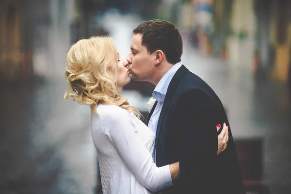 Ο άνθρωπος σε μαύρο σακάκι φιλιά μια σγουρά ξανθιά στέκεται για το υγρό st — Φωτογραφία Αρχείου